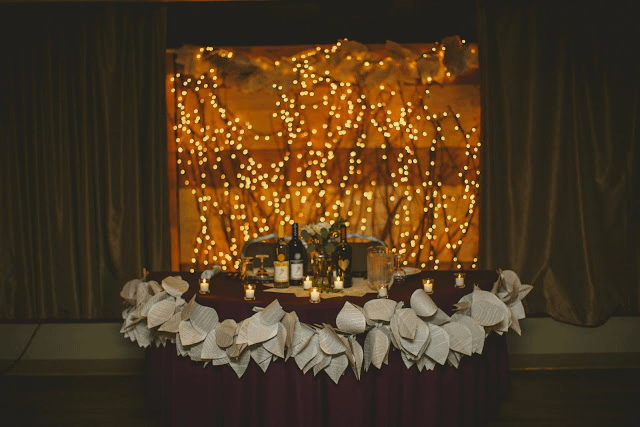 Branches, twinkle light and a garland made of book pages make up this wedding backdrop.
